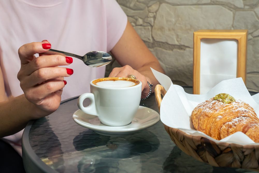 Young woman enjoying cappuccino coffee red manicure hands croissant pastry breakfast morning cafe lifestyle italian cafe culture