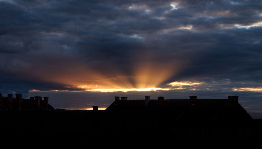 Sun peaking through clouds over houses
