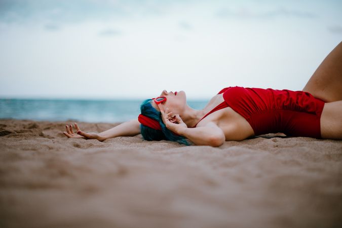 Relaxed woman in bright stylish swimsuit lying on sandy beach
