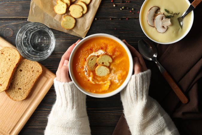 Woman in cosy sweater reaching for bowl of soup