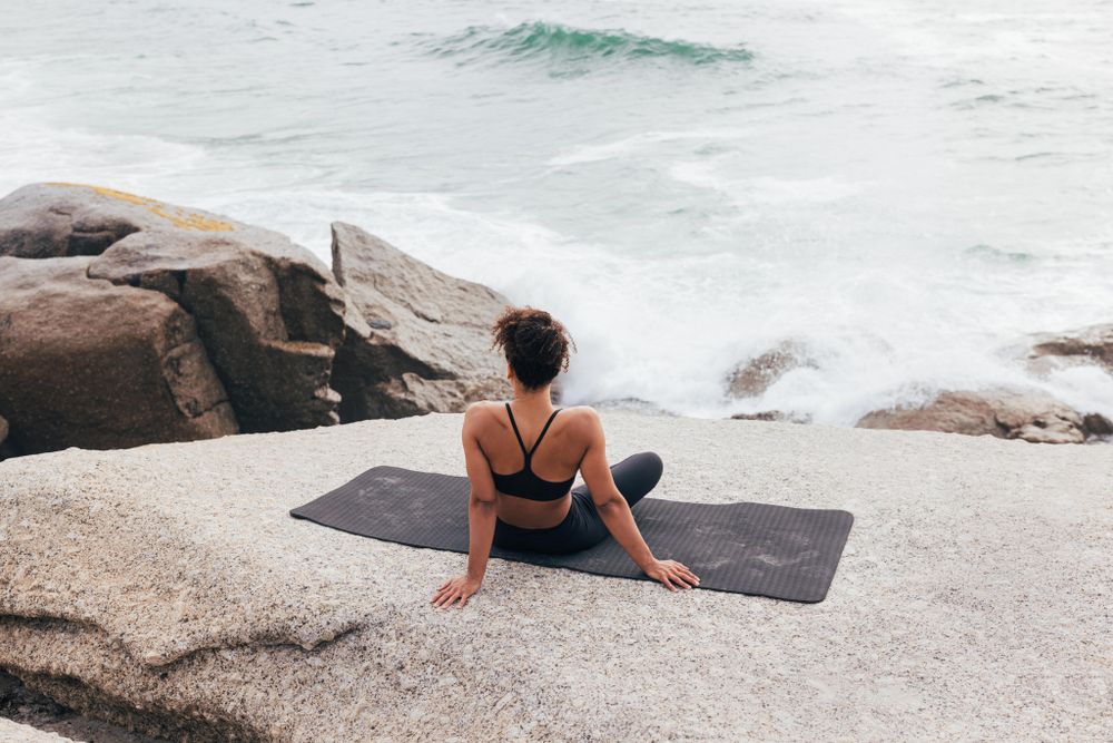 Female sitting next to the ocean sitting with legs crossed
