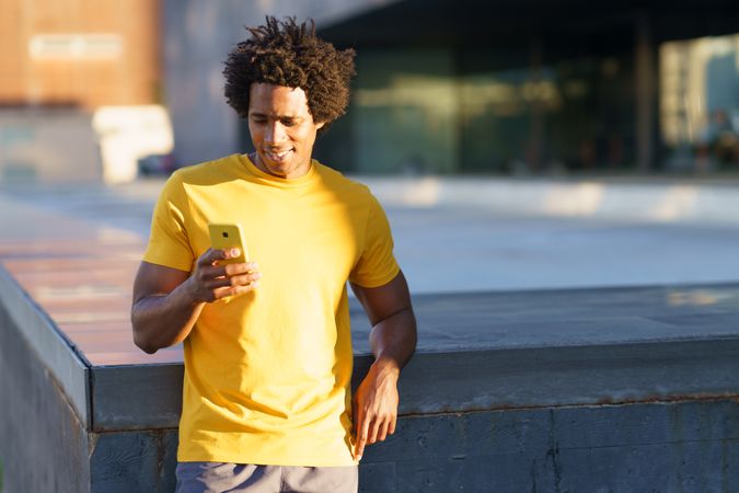 Black man in yellow t-shirt checking his smart phone in the sun