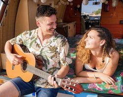 Amorous man plying on guitar and looking at woman in trunk of car