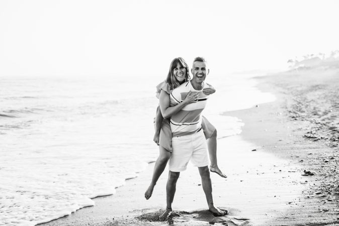 Man carrying woman on back near sea