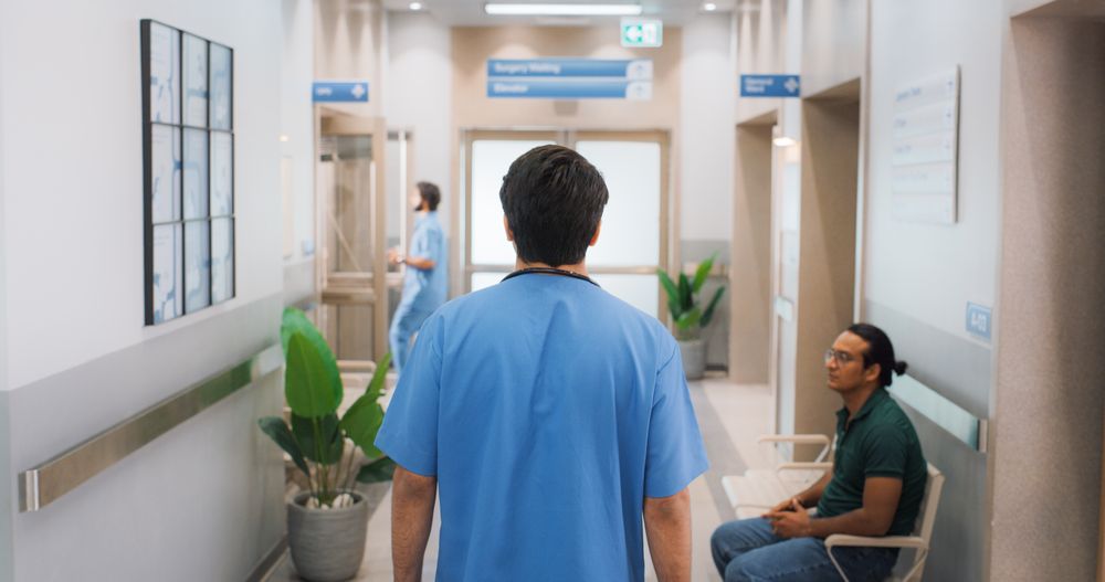 Backview Shot of Young Male Doctor Walking in Hospital Corridor.