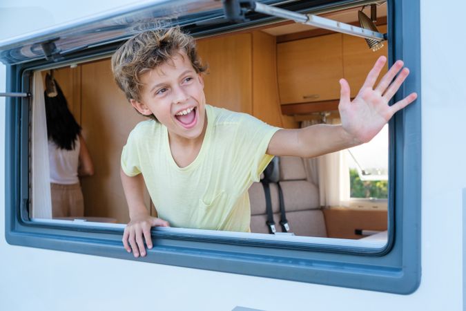 Happy boy waving hand from RV window