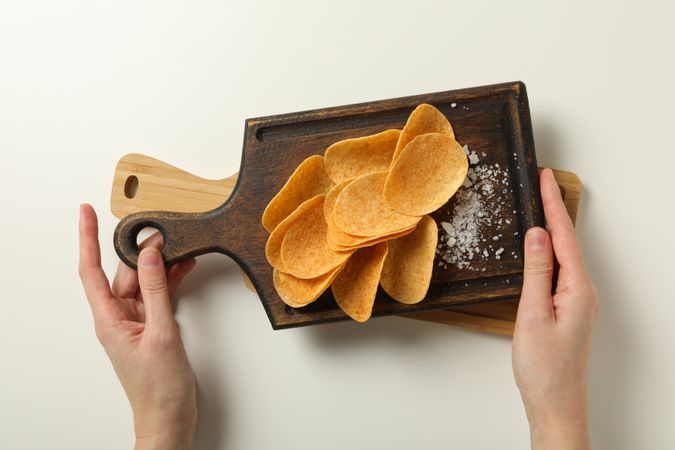 Potato chips on a wooden board with salt on a light background