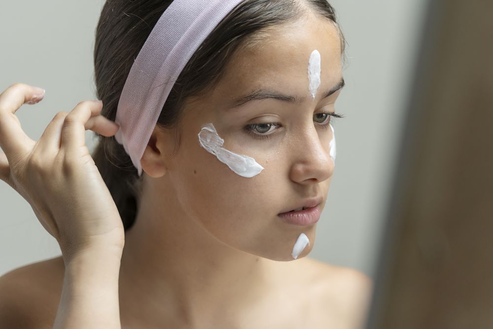 Young woman looking in the mirror, preparing her skin with cream for a beauty routine