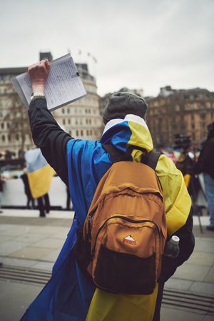 London, England, United Kingdom - March 5 2022: Back of man draped in Ukrainian flag holding up note