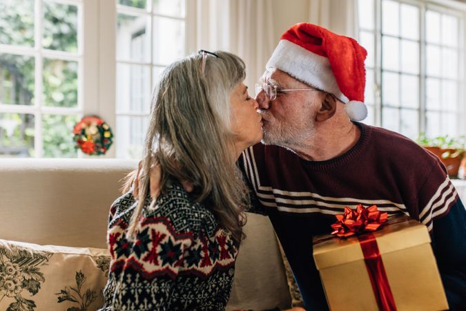 Man in santa cap kissing his wife holding a christmas present