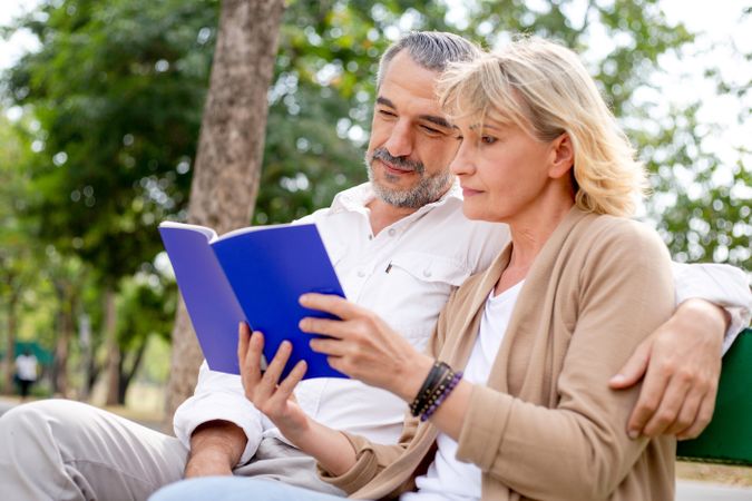 Happy man and woman sitting on park bench reading book at park
