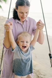 Happy child swinging with mother support while resting on ocean beach