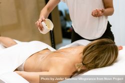 Masseuse pouring oil on back of female client 0LoBRb