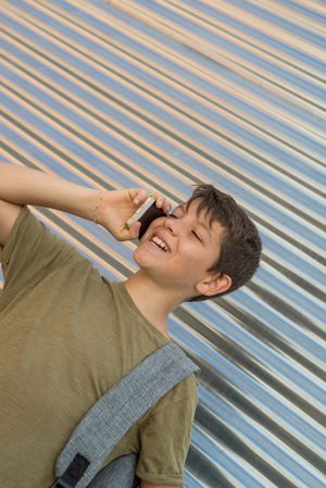 Happy young teenage male speaking on phone in front of shutter
