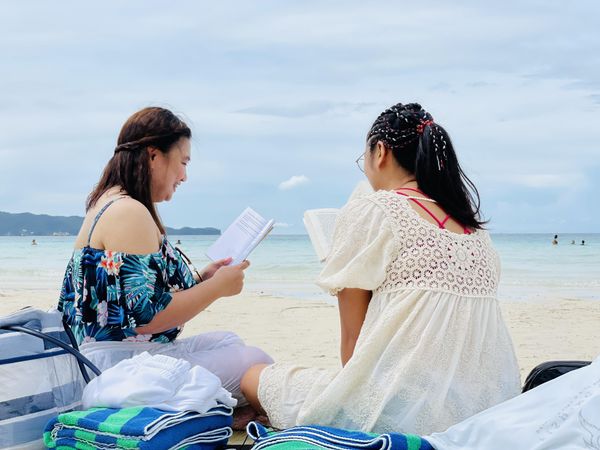 Back view of two women reading on beach