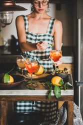 Young woman in checkered dress and glasses holding aperitif with orange slices and olive