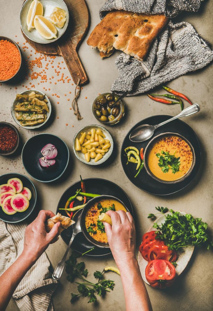 Spread of yellow lentil soup bowls, with bread, vegetable garnishes with man dipping bread into soup