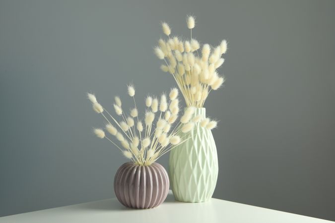 Textured round vase and tall vase filled on table with dried grass in grey room