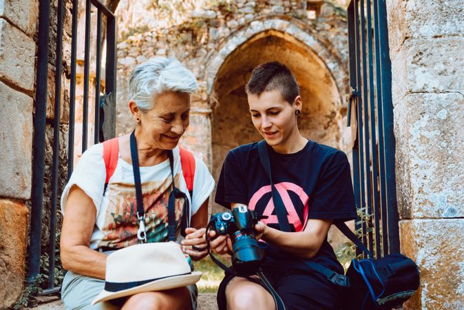 Stylish young woman showing photography to mature woman on stony steps
