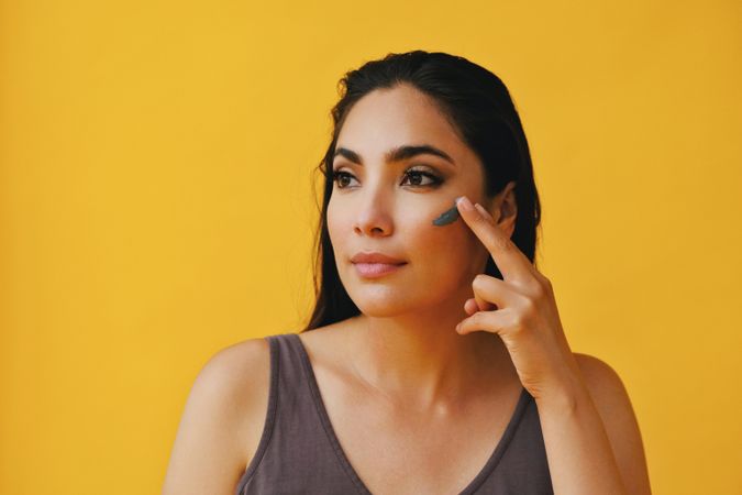 Latina woman applying clay mask with fingers