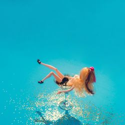Doll bathing in martini glass full of gold glitter on blue background