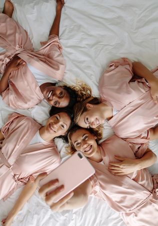 Top view of bride taking selfie with bridesmaids while lying on bed