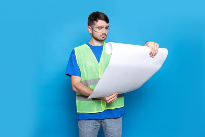 Engineer in glasses with drawing paper in hands on blue background