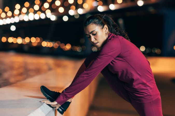 Woman in dark red sportswear stretching in the evening