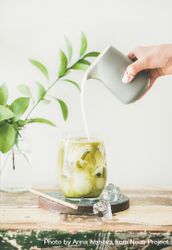 Iced matcha drink with hand pouring cream from grey pitcher 48Mzqb
