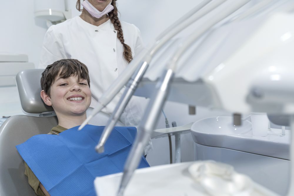 Little boy smiling in the dental office with female dentist standing behind chair