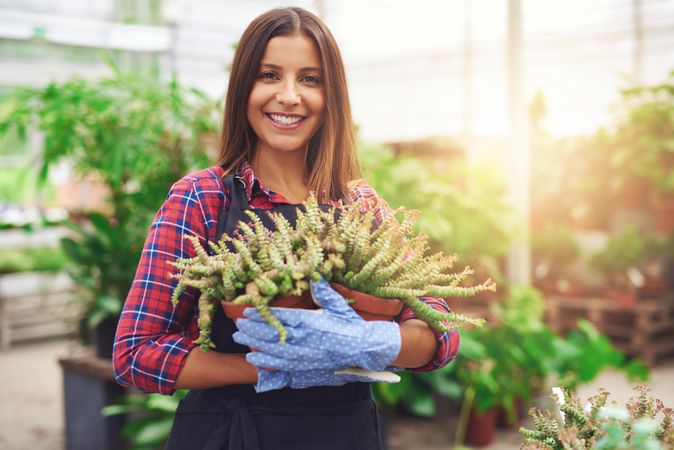 Smiling woman holding two terra-cotta planters in a greenhouse