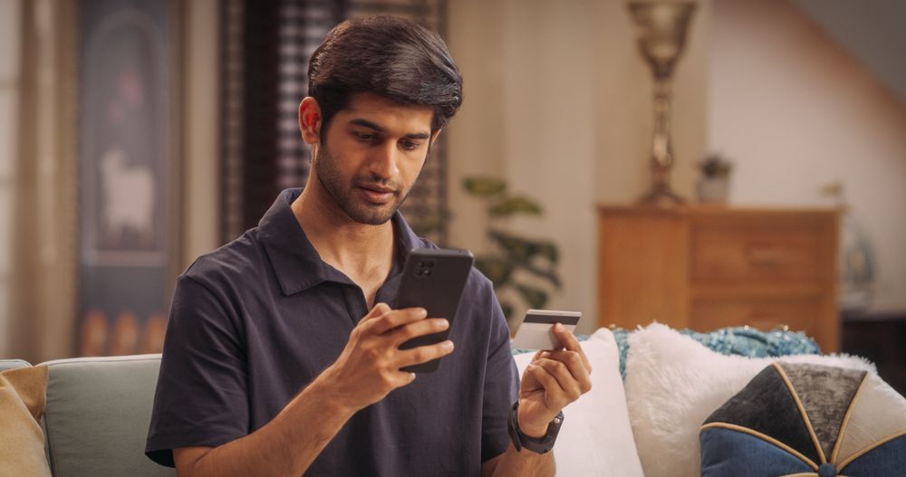 Indian Man Using Smartphone and Credit Card: Effortlessly Navigating Online Shopping, Making Secure Transactions