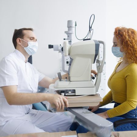 Side view of optometrist looking into patient’s eyes with equipment