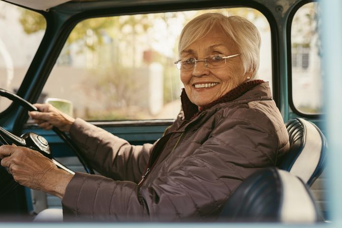 Portrait of beautiful woman with gray hair in warm clothing driving a vintage car