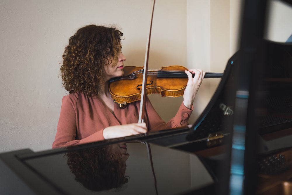 Pregnant woman playing on violin near piano in room