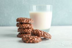 Stack of chocolate cookies with glass of milk on table against light background