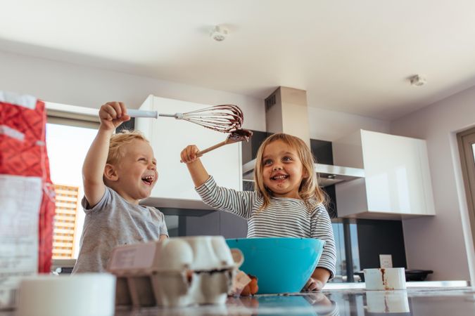 Cute little boy and girl play fighting with whisk and spatula while mixing batter in a bow