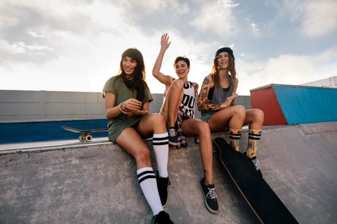 Three women enjoying a day at skate park waving at someone