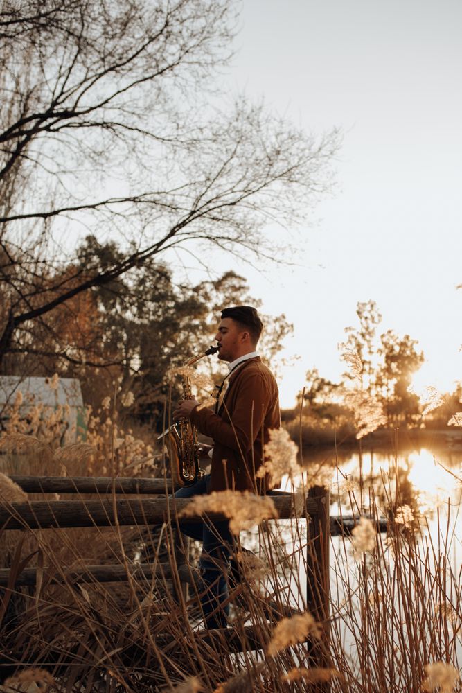 young musician playing the saxophone at sunset in the lake