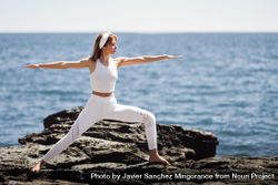 Woman wearing sport clothes and doing warrior B pose on rocks on the coast 4m2RNb