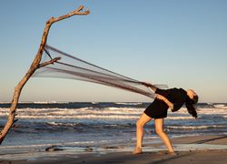 Woman in fishing net fixed on twig near water on shore