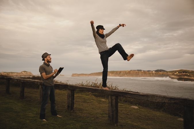 Couple holding hands and jumping on bench on shore near water
