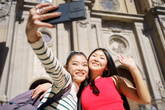 Two cheerful women taking selfie in front of Church in Spain