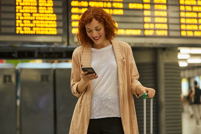Red haired young woman using smartphone at station