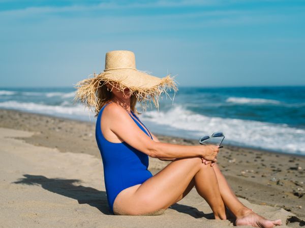 Woman in hat covering face sitting on beach