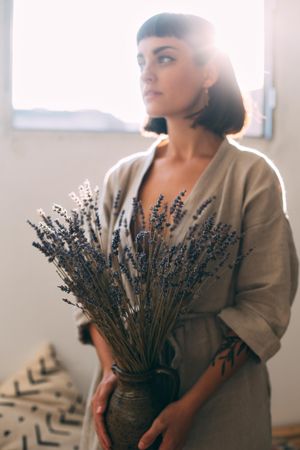Backlit woman in neutral colors holding pot of lavender
