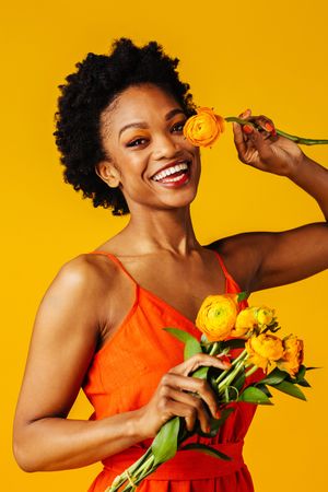 Joyful Black woman playing with ranunculus flowers