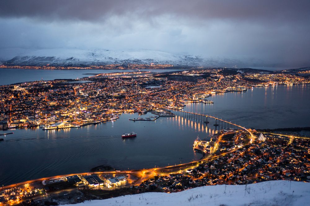 Majestic view of night city against snowy mountains in overcast weather