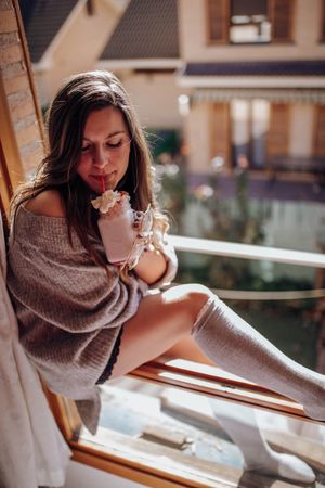Young woman sitting with tasty drink on window