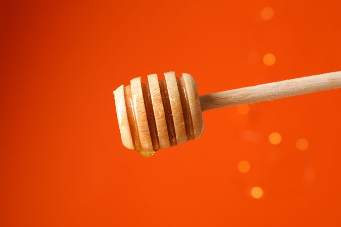 Dipper with honey against orange background with blurred lights, copy space